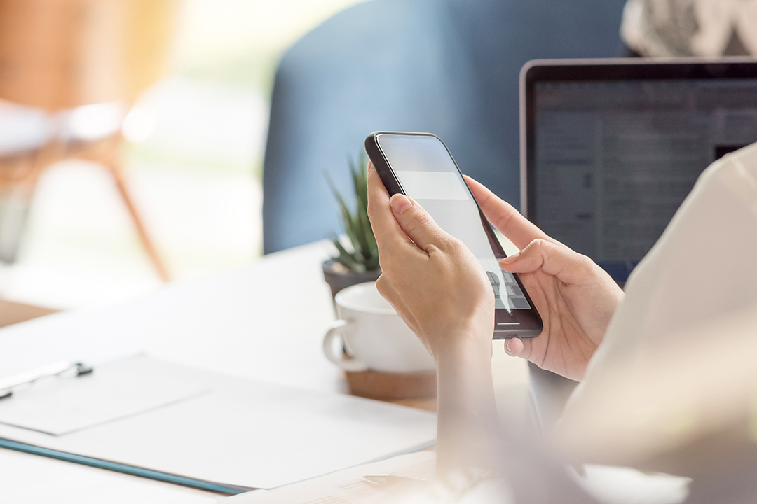 Female hand using smartphone while working at desk in office Alerts and reminders